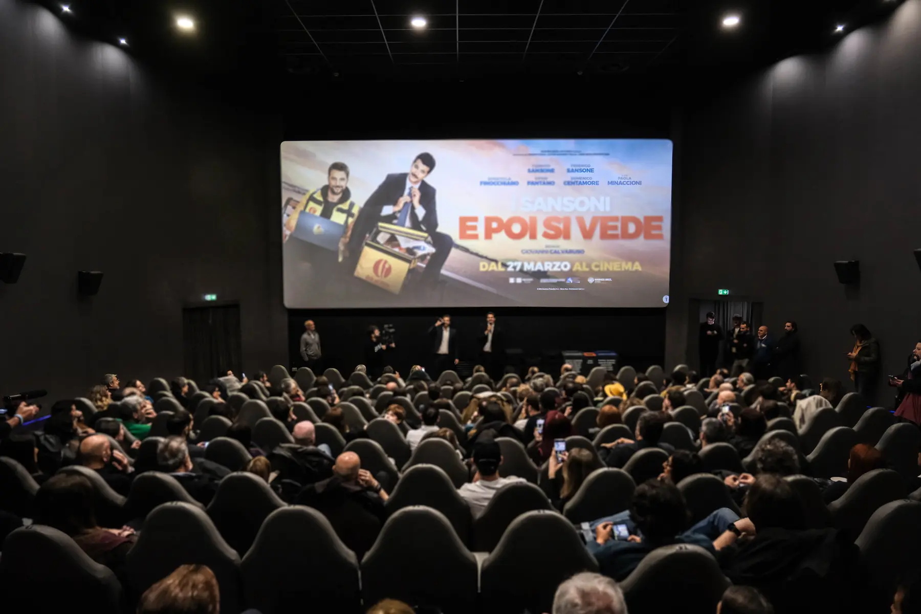 Sala cinematografica piena con la locandina di E poi si vede proiettata sullo schermo